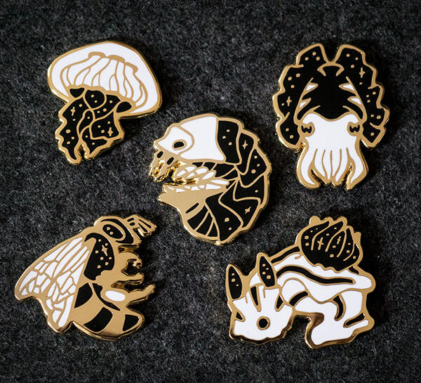 Des pins représentant un isopode, une méduse, une seiche, un nudibranche et une abeille.