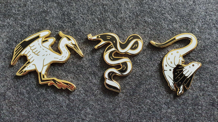 Pins émaillées représentant un héron, une anguille et un lézard.